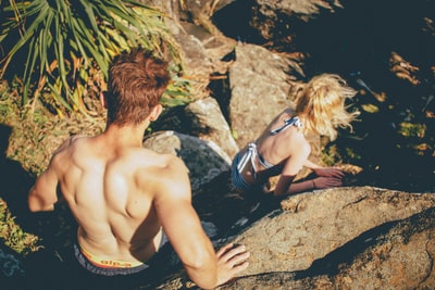 在国王海滩，一对穿着泳衣的夫妇从岩石峭壁上爬下来